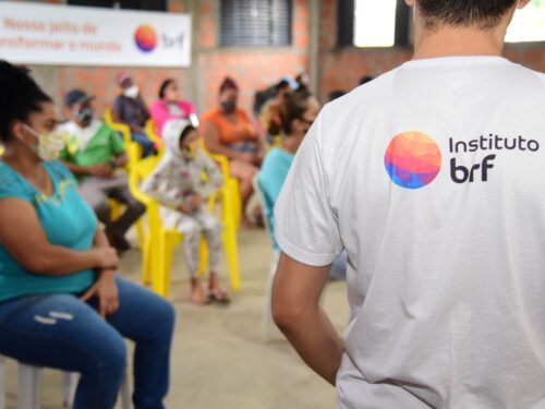 Foto de um homem, em pé, de costas e usando uma camiseta com o logo do Instituto BRF. À sua frente, há um grupo de pessoas sentadas.