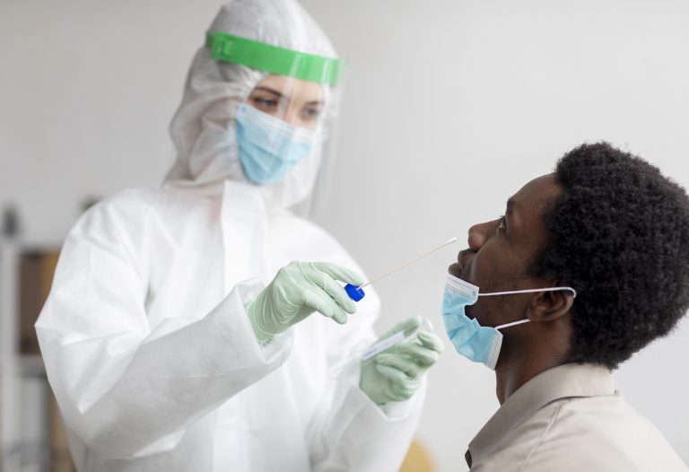 Foto de um homem negro sendo testado para Covid-19 por uma mulher.