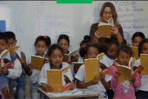 Professora e crianças lendo em conjunto em sala de aula
