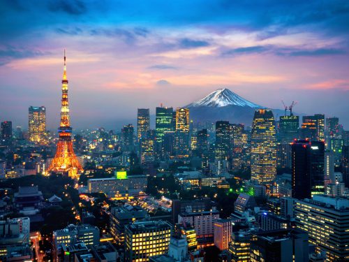 Fotografia colorida que mostra uma cidade do Japão. Em primeiro plano, diversos prédios modernos. Ao fundo, o monte Fuji.