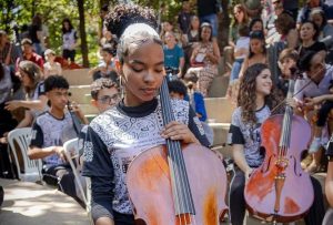 menina tocando violoncelo junto com orquestra social